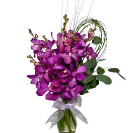 Purple orchids in a clear glass vase with a silver ribbon