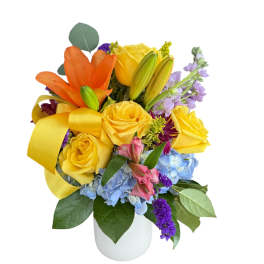 Bouquet of yellow and orange roses with blue hydrangeas in a white vase