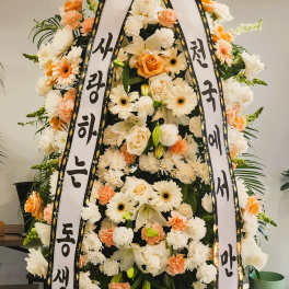 Tall white and peach standing spray with roses, lilies, gerberas, and Korean message ribbons on an easel