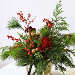 Holiday arrangement with red roses, pine, and red berries in a vase