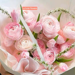 Pink ranunculus bouquet wrapped in pale pink paper with a white ribbon