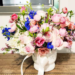 Pink and blue mixed flower arrangement in a white vase with ribbon