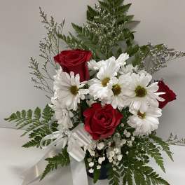 Red roses and white daisies in a vase with a white ribbon