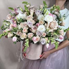 Large pastel arrangement of roses, tulips, and orchids in a blush hatbox held by a person
