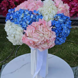 Bouquet of pink, blue, and white hydrangeas in a tall white vase