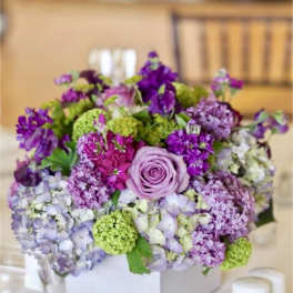 Lavender and purple floral arrangement in a white box on a table