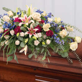 Large floral spray with white roses, lilies, and blue flowers on a wooden casket