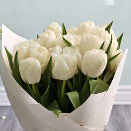Bouquet of white tulips wrapped in white paper in a glass vase