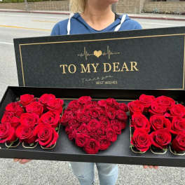 Black gift box with red roses arranged in a heart shape