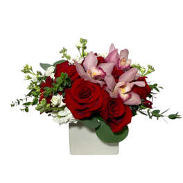 Red roses and pink orchids in a white square vase