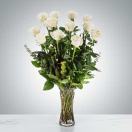 White roses arranged in a clear glass vase with greenery