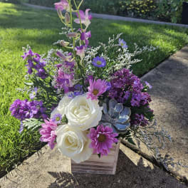 Purple and white floral arrangement in a wooden box with a succulent