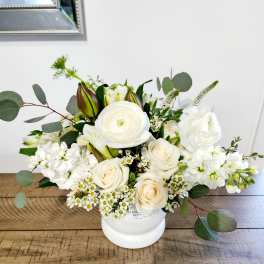 White floral arrangement in a white vase with roses and ranunculus