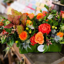 Orange and red rose arrangement in a green rectangular container