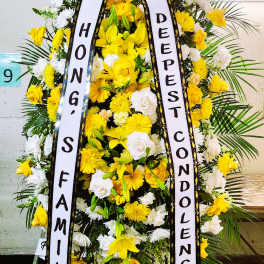 Tall yellow and white standing funeral spray with condolence ribbons on an easel.
