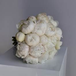 Round hand-tied bouquet of ivory peonies resting on a white pedestal