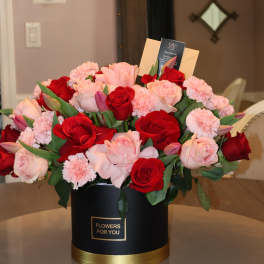 Bouquet of red and blush roses with pink carnations in a black hatbox