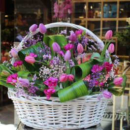 Pink tulips and small purple flowers in a white wicker basket
