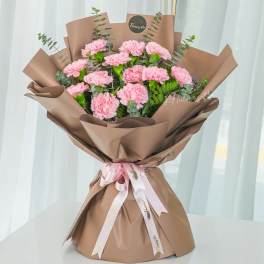 Pink carnation bouquet wrapped in brown paper with a ribbon