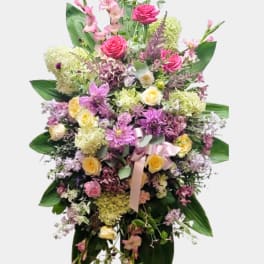 Tall standing floral spray with pink and yellow flowers and a ribbon