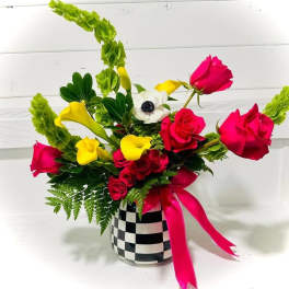 Bouquet of pink roses and yellow calla lilies in a checkered vase with a pink ribbon