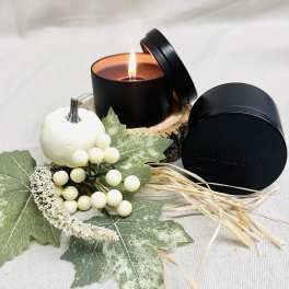 Black candle tin with a lit candle and autumn decor accents