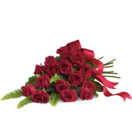 Cluster of red roses with fern fronds and a red ribbon in a flat bouquet