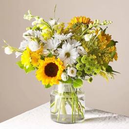 Mixed bouquet of sunflowers, white daisies, and yellow blooms in a glass vase