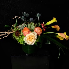 Arrangement of peach roses and yellow calla lilies in a dark vase