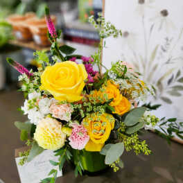 Yellow roses and mixed flowers arranged in a green vase