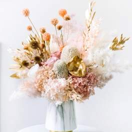 Dried floral arrangement in a white vase with blush and gold accents