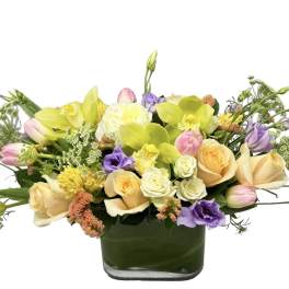Low arrangement of pastel roses, tulips, orchids, and lisianthus in a rectangular glass vase