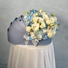 Light blue cradle-shaped box filled with white and blue flowers and a small baby figurine.