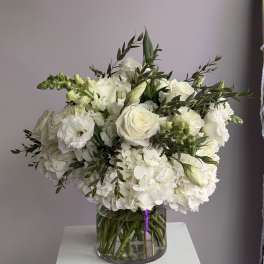 Round arrangement of white roses, hydrangeas, and other white blooms in a clear glass vase