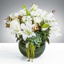 White lilies and roses with succulents arranged in a round green glass vase