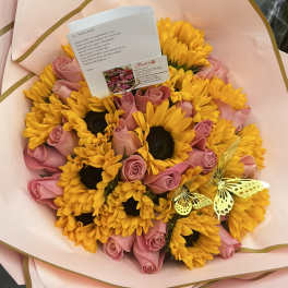 Bouquet of yellow sunflowers and pink roses wrapped in pale pink paper