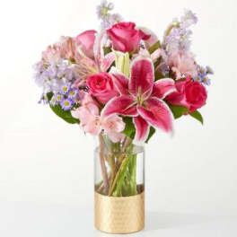 Pink roses and lilies in a clear glass vase with a gold wrap