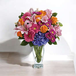 Mixed bouquet of pink, orange, and blue flowers in a clear glass vase