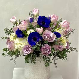 Pink tulips, lavender roses, and blue anemones in a white vase