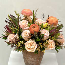 Peach and blush roses with orange ranunculus in a rustic vase