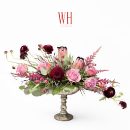 Pink and burgundy floral arrangement in a silver pedestal vase