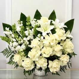 White floral arrangement in a woven basket with dark green leaves