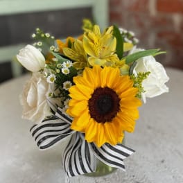 Sunflower bouquet with white tulips and a black-and-white striped ribbon in a glass vase