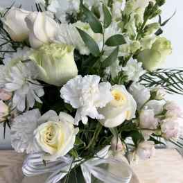 White roses and chrysanthemums in a glass vase with a ribbon