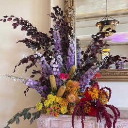 Large floral arrangement with purple, yellow, and red blooms in a decorative indoor setting
