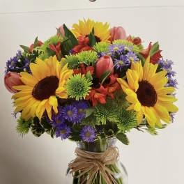 Bright mixed bouquet with sunflowers, tulips, and purple daisies in a glass vase