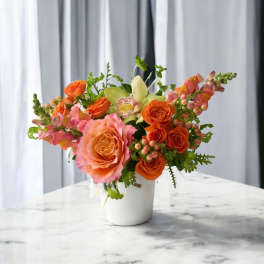 Compact arrangement of orange roses, pink blooms, and a green orchid in a white vase