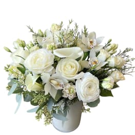 White floral arrangement in a pale vase with roses, calla lilies, and orchids