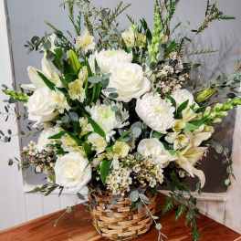 White floral arrangement in a woven basket with roses and lilies