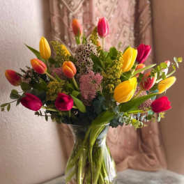 Clear glass vase of yellow, orange, and red tulips mixed with small filler flowers on a tabletop